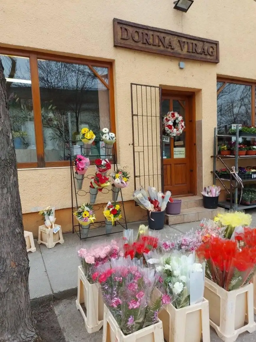 A bolt bejárata a faragott Dorina Virág cégtáblával, előtte kész csokrok és vágott virág vödrökben