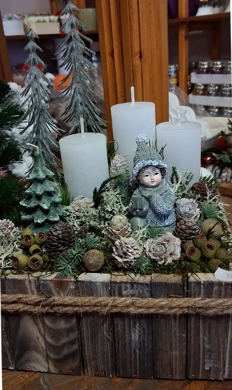 Karácsonyi asztaldísz fadobozban: fehér gyertyák, zúzmarás fenyők, tobozok és egy téli figura